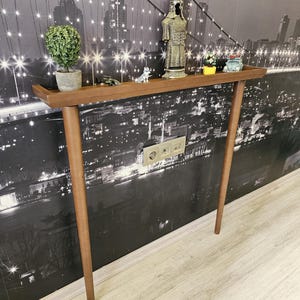 May include: A mid-century modern style console table with a brown wooden top and legs. The table is decorated with small figurines and a potted plant. The background is a black and white cityscape.
