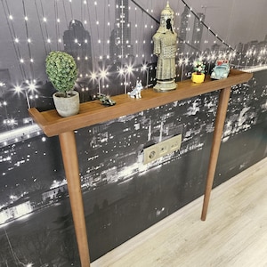 May include: A brown wooden console table with a rectangular top and four tapered legs. The table is decorated with small figurines, including a plant in a pot, a soldier statue, and a toy car. The background is a black and white cityscape.