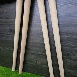 K&ouml;nnte beinhalten: Vier unfertige Tischbeine aus Holz mit Metallmontageplatten. Die Beine sind hell, konisch und zylindrisch und f&uuml;r den M&ouml;belbau bestimmt. Die Beine sind etwa 61 cm lang.