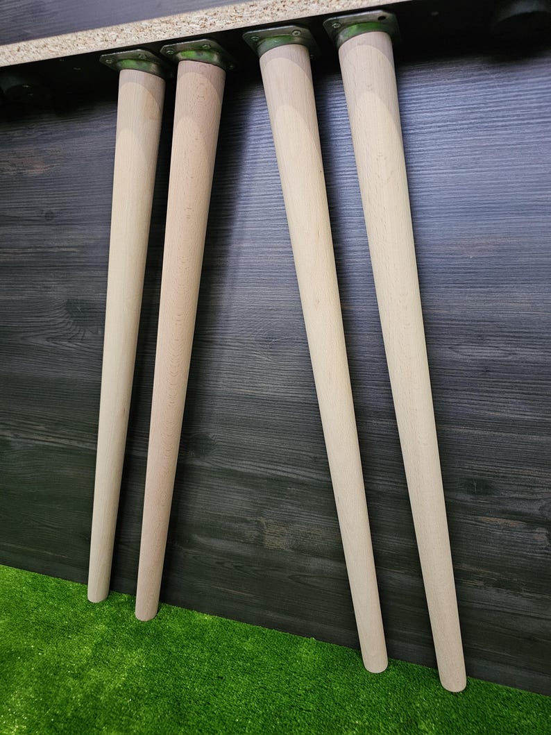 K&ouml;nnte beinhalten: Vier unfertige Tischbeine aus Holz mit Metallmontageplatten. Die Beine sind hell, konisch und zylindrisch und f&uuml;r den M&ouml;belbau bestimmt. Die Beine sind etwa 61 cm lang.