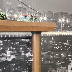 May include: A light blue toy car with a red surfboard on top sits on a wooden shelf. The shelf is supported by a brown wooden leg. The background is a black and white cityscape with a bridge.
