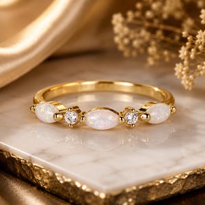 May include: A gold ring featuring three marquise-cut opals and two round-cut clear stones arranged in an alternating pattern along the band. The metal band is polished gold, and the stones are set in a horizontal row across the center of the ring.
