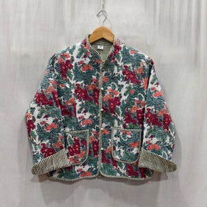 Può includere: Giacca trapuntata con motivo floreale nei toni del rosso, verde e pesca su sfondo bianco. Presenta un colletto alla coreana, chiusura con bottoni e due tasche frontali. I polsini e i bordi presentano un motivo a righe bianche e nere.
