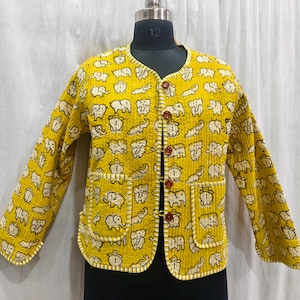 May include: A yellow quilted jacket with a repeating pattern of white elephants. The jacket has a round collar, long sleeves, two front pockets, and brown buttons. The edges are trimmed with white stitching.