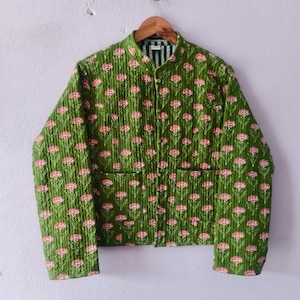 May include: Green quilted jacket featuring a pink and white floral design. The jacket has a mandarin collar, two front pockets, and a striped lining. It is displayed on a wooden hanger.