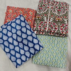 May include: Four folded fabric pieces with floral and leaf patterns. One fabric is blue with white leaves, another is pink with orange flowers, a third is white with pink flowers and green leaves, and the last is white with green and yellow leaves.