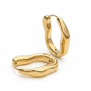 May include: A pair of gold-toned hoop earrings featuring an irregular, organic, and wavy surface texture. One earring is positioned upright in a vertical orientation, while the other rests horizontally on its side, showcasing the continuous metal loop.