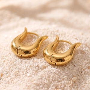 May include: A pair of polished gold hoop earrings featuring a smooth, curved U-shape design. The earrings have a thick, rounded profile with a hinged closure mechanism, showcasing a reflective metallic finish that catches the light.