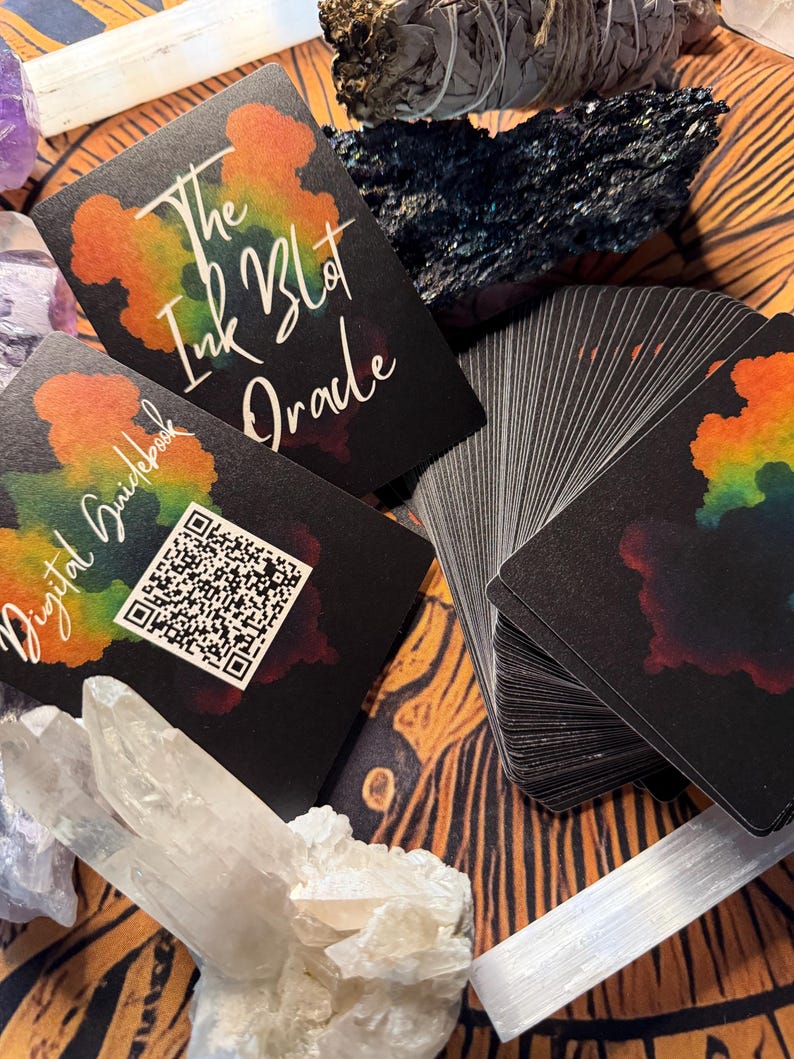 Pu&ograve; includere: Un mazzo di carte oracolo nere con un design a macchia di inchiostro colorato, intitolato "The Ink Blot Oracle". L'immagine include una guida con un codice QR, cristalli e altri oggetti spirituali. Le carte sono a ventaglio, mostrando i loro bordi.