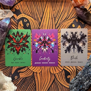 Pu&ograve; includere: Tre carte dei tarocchi con disegni simmetrici e testo. Le carte sono etichettate "Gamble", "Creativity" e "Death". La carta Gamble &egrave; verde con accenti rossi e neri. La carta Creativity &egrave; viola con schizzi di vernice colorati. La carta Death &egrave; grigia con inchiostro nero.