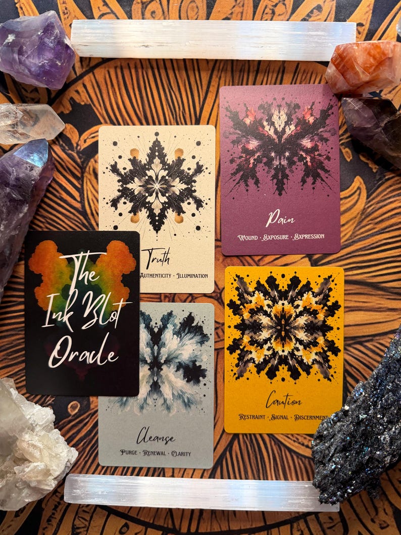 Pu&ograve; includere: Una vista dall'alto delle carte Oracle The Ink Blot con cristalli. Le carte presentano disegni astratti di macchie di inchiostro in nero, viola e giallo. Il testo sulle carte include "Truth", "Pain", "Cleanse" e "Caution". Cristalli di ametista, selenite e quarzo circondano le carte.
