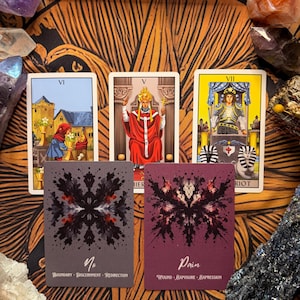 Pu&ograve; includere: Un gruppo di carte dei tarocchi con illustrazioni colorate e testo. Le carte raffigurano varie scene e simboli, tra cui figure, edifici e disegni astratti. Le carte sono disposte su una superficie a motivi, circondate da cristalli e altri elementi decorativi.