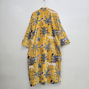May include: Mustard yellow kimono-style robe with a jungle-themed pattern. The robe features a repeating design of zebras, leopards, toucans, and palm trees. The robe is hanging on a wooden hanger against a plain white wall.