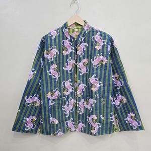 May include: A long-sleeved jacket with a mandarin collar, featuring a repeating pattern of pink tigers on a striped background of blue and green. The jacket has a button closure and two front pockets, hanging on a wooden hanger.