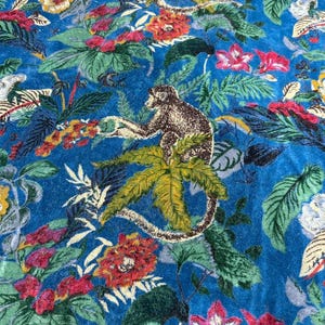 Könnte beinhalten: Ein lebendiger blauer Stoff mit einem Dschungel-Thema. Das Muster zeigt Affen, üppiges grünes Laub und bunte Blumen in Rot-, Gelb- und Weißtönen. Die Gesamtästhetik erinnert an ein tropisches Paradies.