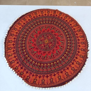 Peut inclure: Tapisserie ronde ornée de motifs rouges, oranges et verts. Le motif répète des éléments animaliers et floraux, bordés de pompons blancs. Ce textile décoratif est adapté à divers usages.