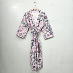 May include: A floral print robe in shades of pink, green, and purple hangs on a wooden hanger. The robe is tied at the waist and features a quilted design. The robe is made of a soft, lightweight fabric.