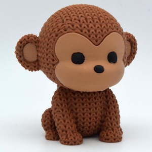 May include: A brown monkey figurine with a knitted texture. The monkey has a light brown face, ears, and hands, with black eyes. The figurine is sitting on its haunches, with its arms resting on its legs.
