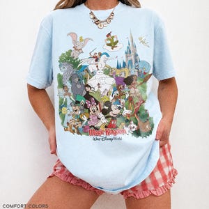 Peut inclure: T-shirt bleu clair avec un motif color&eacute; de personnages Disney, dont Mickey Mouse, Dumbo et Peter Pan. Le texte "Magic Kingdom Our Disney World" est imprim&eacute; sur le devant. Le t-shirt est en tissu chambray.