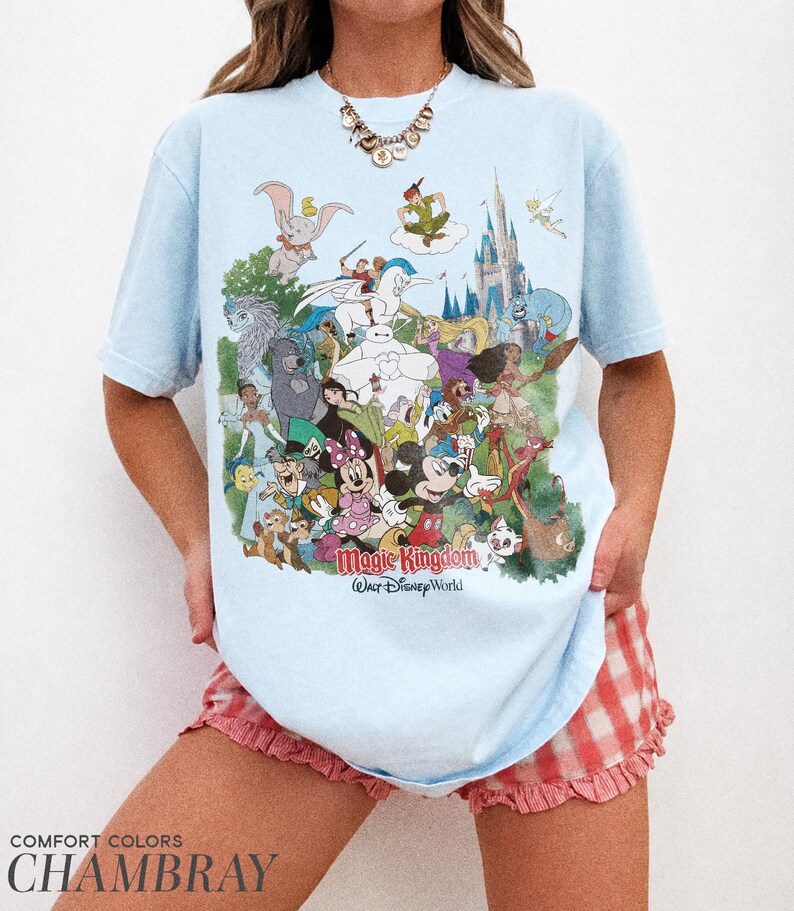 Peut inclure: T-shirt bleu clair avec un motif color&eacute; de personnages Disney, dont Mickey Mouse, Dumbo et Peter Pan. Le texte "Magic Kingdom Our Disney World" est imprim&eacute; sur le devant. Le t-shirt est en tissu chambray.
