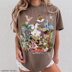 Peut inclure: T-shirt couleur expresso avec un graphisme color&eacute; de personnages Disney, dont Mickey Mouse, Dumbo et Peter Pan. Le graphisme comprend les mots "Magic Kingdom" et "Walt Disney World". Le t-shirt est de la marque Comfort Colors.