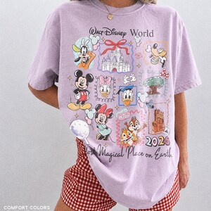 May include: A light purple t-shirt with a Walt Disney World graphic featuring Mickey Mouse, Minnie Mouse, Donald Duck, and other characters. The shirt also has the text "Most Magical Place on Earth" and "2026".