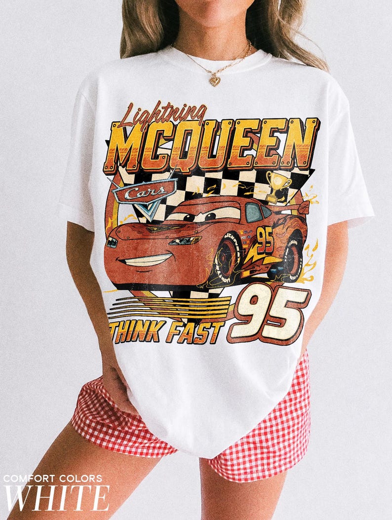 K&ouml;nnte beinhalten: Wei&szlig;es T-Shirt mit einem Aufdruck von Lightning McQueen aus dem Film Cars. Das Design enth&auml;lt die Texte "Lightning McQueen", "Cars", "95" und "Think Fast". Das T-Shirt hat einen Vintage-Look.