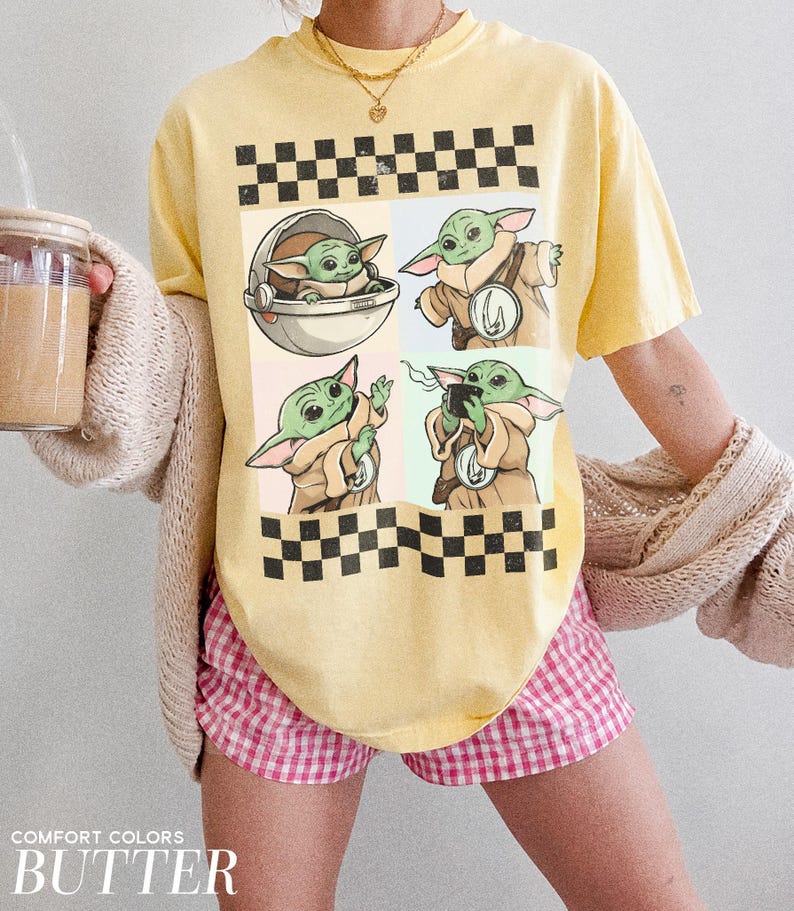 Puede incluir: Camiseta amarilla con un dise&ntilde;o gr&aacute;fico de Grogu de The Mandalorian en cuatro paneles, sobre un patr&oacute;n de tablero de ajedrez. La camiseta tiene las palabras "COMFORT COLORS" y "BUTTER" impresas en la parte inferior. La persona lleva un pantal&oacute;n corto a cuadros rosa y blanco.