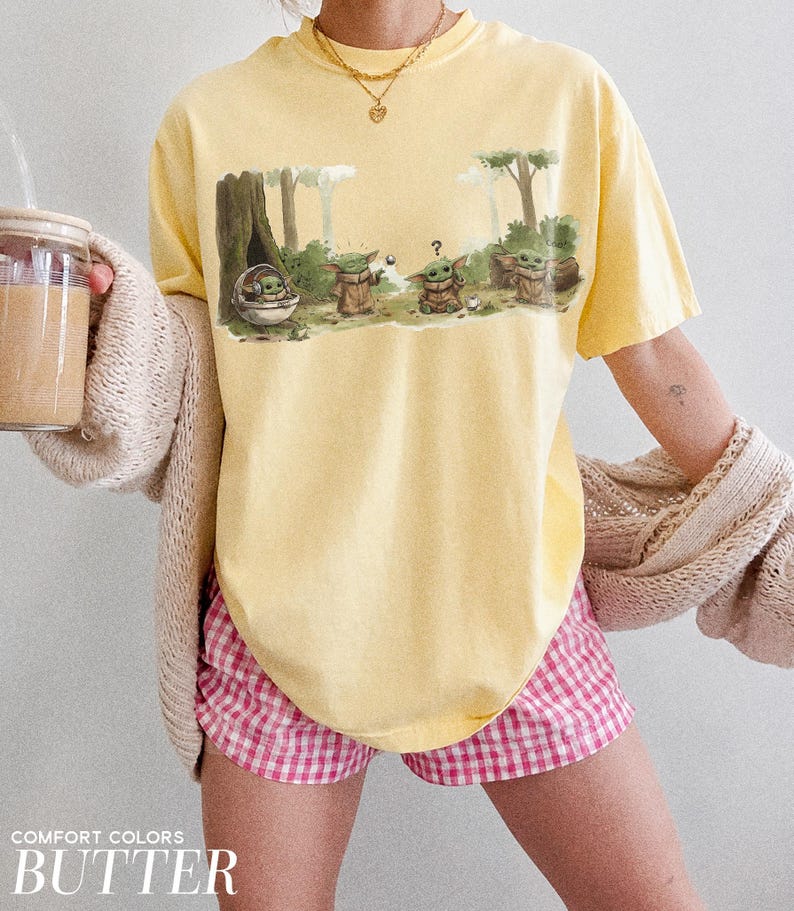 May include: Yellow Comfort Colors t-shirt with a graphic of Grogu from The Mandalorian. The graphic shows Grogu in a pod and with other characters in a forest scene. The shirt is paired with pink and white checkered shorts.