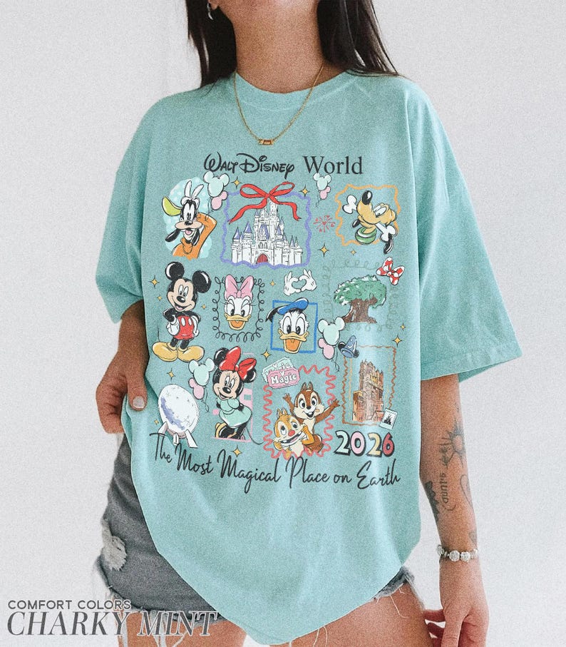 May include: A light blue t-shirt with a graphic featuring various Disney characters and the text "Walt Disney World" and "The Most Magical Place on Earth 2026". The shirt is labeled "Comfort Colors" and "Charky Mint".