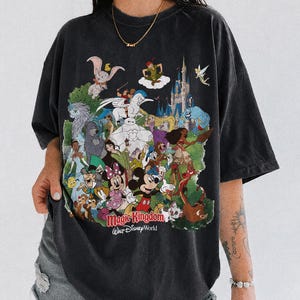 Peut inclure: T-shirt noir avec un graphisme color&eacute; de personnages Disney, dont Mickey Mouse et des princesses, et le texte "Magic Kingdom Walt Disney World". Le t-shirt porte &eacute;galement le texte "COMFORT COLORS BLACK."