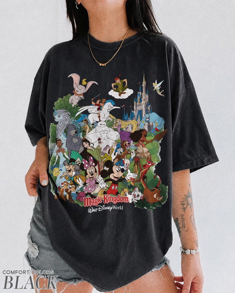 Peut inclure: T-shirt noir avec un graphisme color&eacute; de personnages Disney, dont Mickey Mouse et des princesses, et le texte "Magic Kingdom Walt Disney World". Le t-shirt porte &eacute;galement le texte "COMFORT COLORS BLACK."