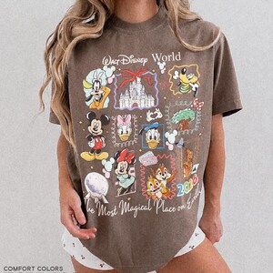May include: Espresso-colored t-shirt featuring a collage of Disney characters and the text "Walt Disney World" and "The Most Magical Place on Earth." The design includes Mickey Mouse, Minnie Mouse, Donald Duck, and Goofy. The year 2016 is also visible.