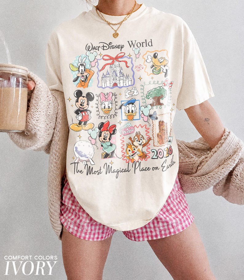 May include: Ivory-colored t-shirt featuring a colorful graphic of Disney characters and the text "Walt Disney World" and "The Most Magical Place on Earth". The shirt is paired with pink and white checkered shorts.