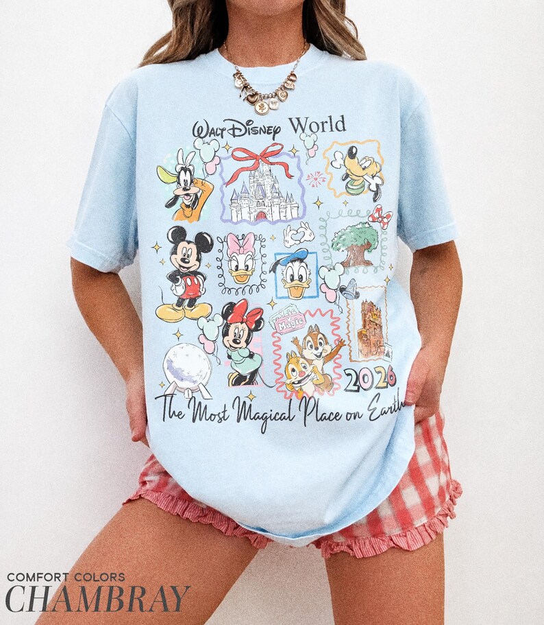 May include: Light blue t-shirt featuring Disney characters and the text "Walt Disney World" and "The Most Magical Place on Earth". The shirt has a 2026 graphic and is made of chambray fabric.