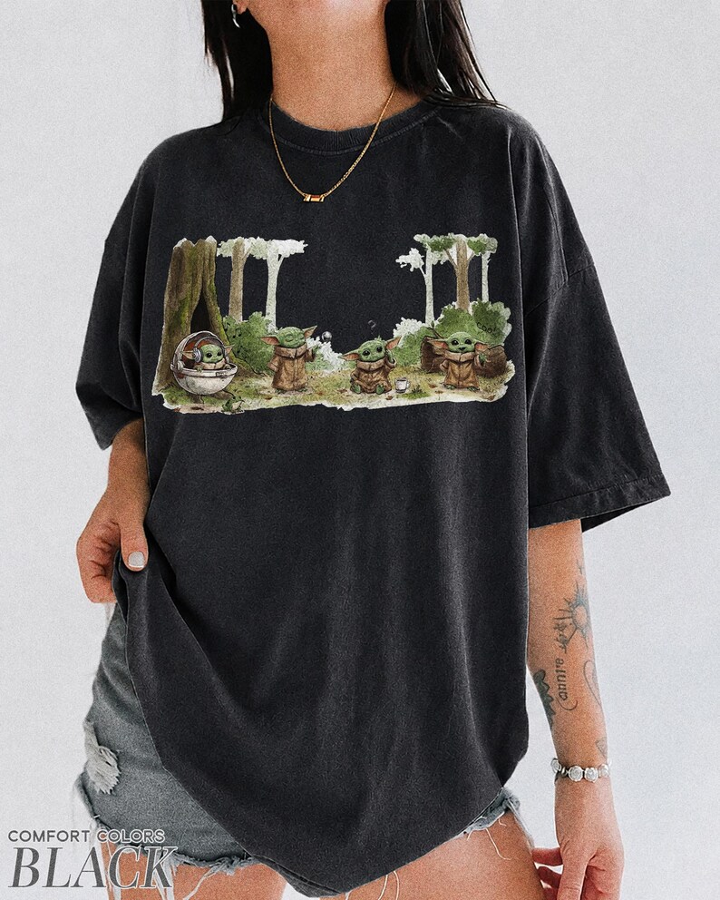 May include: Black t-shirt featuring a graphic of a character from a popular science fiction series. The design shows the character in a forest setting. The words "COMFORT COLORS BLACK" are printed at the bottom of the shirt.