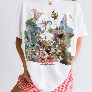 Peut inclure: T-shirt blanc avec un motif color&eacute; de personnages Disney, dont Mickey Mouse, Peter Pan et Dumbo, avec le texte "Magic Kingdom Walt Disney World." Le t-shirt est de la marque Comfort Colors.