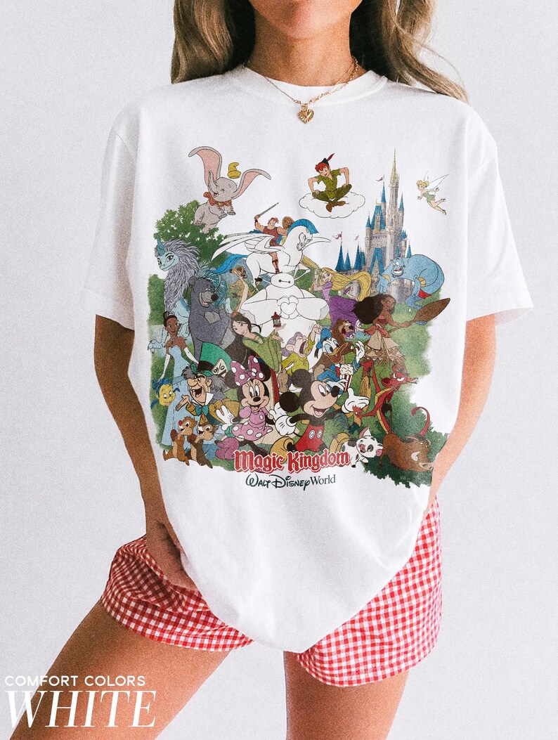 Peut inclure: T-shirt blanc avec un motif color&eacute; de personnages Disney, dont Mickey Mouse, Peter Pan et Dumbo, avec le texte "Magic Kingdom Walt Disney World." Le t-shirt est de la marque Comfort Colors.