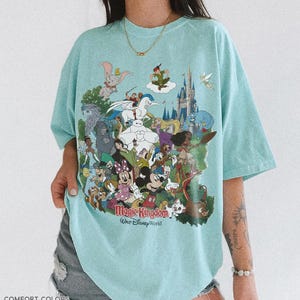 Peut inclure: T-shirt bleu clair avec un motif color&eacute; de personnages Disney, dont Mickey Mouse, Dumbo et Peter Pan. Le texte "Magic Kingdom Walt Disney World" est imprim&eacute; sur le devant. Le t-shirt est &eacute;tiquet&eacute; "Comfort Colors Charky Mint".
