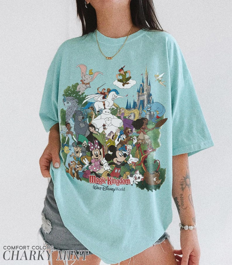 Peut inclure: T-shirt bleu clair avec un motif color&eacute; de personnages Disney, dont Mickey Mouse, Dumbo et Peter Pan. Le texte "Magic Kingdom Walt Disney World" est imprim&eacute; sur le devant. Le t-shirt est &eacute;tiquet&eacute; "Comfort Colors Charky Mint".