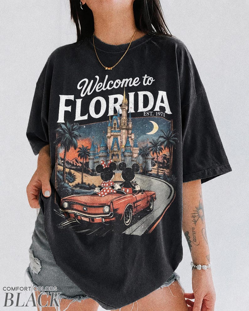 May include: Black t-shirt with a graphic featuring Mickey and Minnie Mouse in a red convertible, driving towards a castle under a moonlit sky. The text "Welcome to FLORIDA EST. 1971" is printed above the graphic.