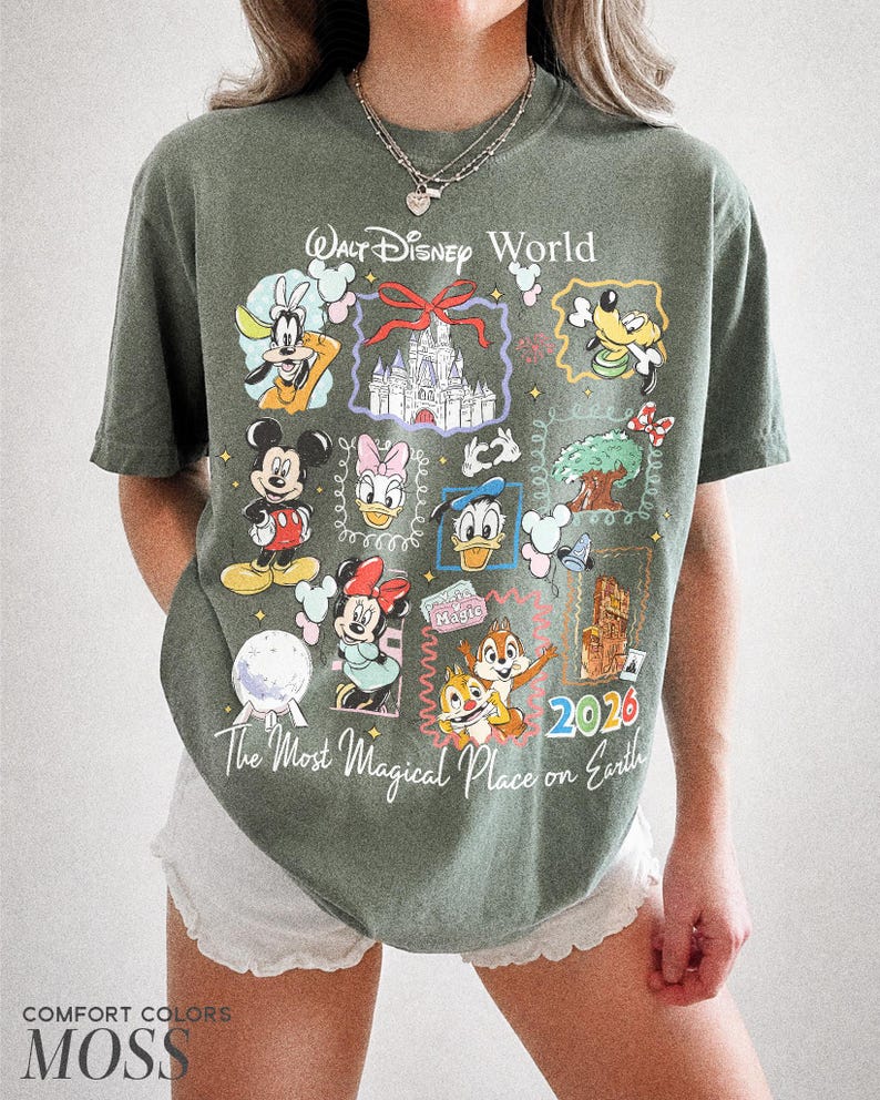 May include: Moss green t-shirt with a Walt Disney World graphic. The design includes various Disney characters and the text "The Most Magical Place on Earth" and "2026". The shirt is made by Comfort Colors.