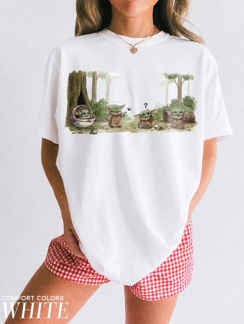 May include: White t-shirt featuring a watercolor illustration of a character from a popular science fiction series. The graphic shows the character in a forest setting with trees and foliage. The text "COMFORT COLORS WHITE" is printed at the bottom.