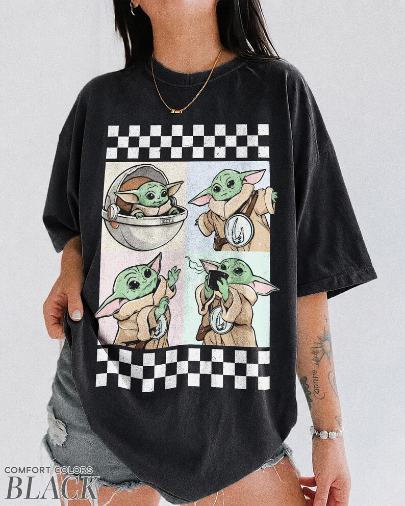 Puede incluir: Camiseta negra con un dise&ntilde;o gr&aacute;fico de cuatro paneles de un personaje alien&iacute;gena verde en varias poses. El dise&ntilde;o est&aacute; enmarcado por un patr&oacute;n de cuadros blancos y negros. Las palabras "COMFORT COLORS" y "BLACK" est&aacute;n impresas en la parte inferior.