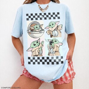 Puede incluir: Camiseta azul claro con un dise&ntilde;o gr&aacute;fico de un personaje alien&iacute;gena verde en cuatro poses diferentes. El dise&ntilde;o incluye un patr&oacute;n de cuadros y el texto "COMFORT COLORS CHAMBRAY" en la parte inferior.
