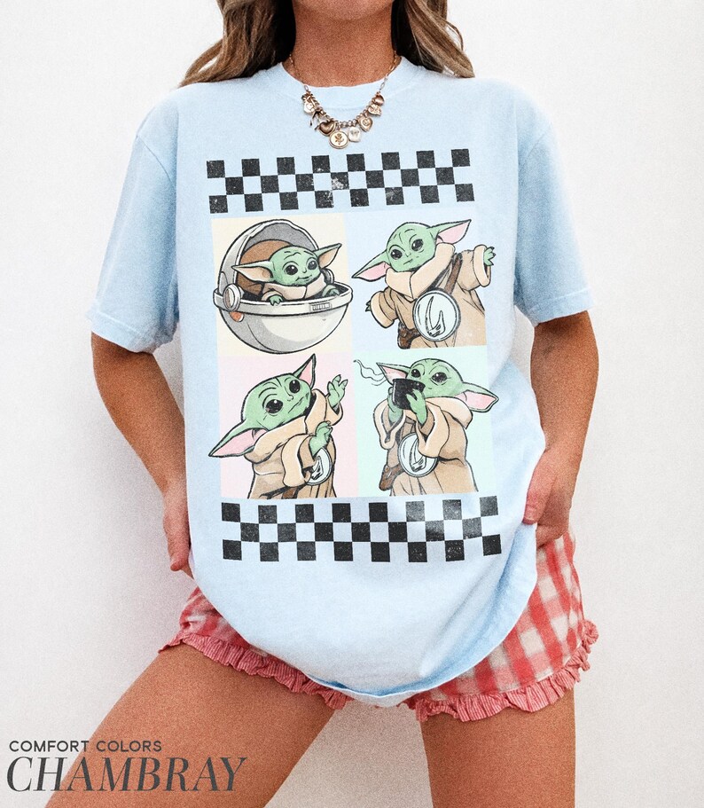 Puede incluir: Camiseta azul claro con un dise&ntilde;o gr&aacute;fico de un personaje alien&iacute;gena verde en cuatro poses diferentes. El dise&ntilde;o incluye un patr&oacute;n de cuadros y el texto "COMFORT COLORS CHAMBRAY" en la parte inferior.