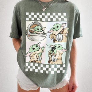 Puede incluir: Camiseta verde Comfort Colors con un dise&ntilde;o de Grogu en cuatro poses diferentes. El dise&ntilde;o est&aacute; sobre un fondo a cuadros blanco y negro. El texto "COMFORT COLORS MOSS" est&aacute; impreso en la parte inferior.