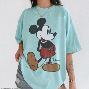 K&ouml;nnte beinhalten: Hellblaues T-Shirt mit einer gro&szlig;en Grafik von Mickey Mouse in seiner klassischen Pose. Das Disney-Logo ist sichtbar. Das Shirt ist unten mit "Comfort Colors" und "Charky Mint" beschriftet.