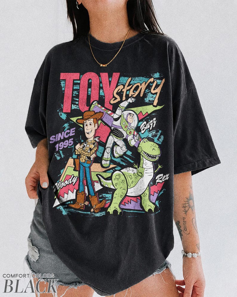 May include: Black Comfort Colors t-shirt featuring a graphic of Woody, Buzz Lightyear, and Rex from Toy Story. The design includes the text "TOY STORY" and "SINCE 1995". The shirt has a vintage, distressed look.