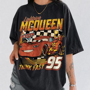 K&ouml;nnte beinhalten: Schwarzes T-Shirt mit Lightning McQueen aus dem Film Cars. Das Design enth&auml;lt die Texte "Lightning McQueen", "Cars", "95" und "Think Fast". Das T-Shirt hat einen Vintage-Look.
